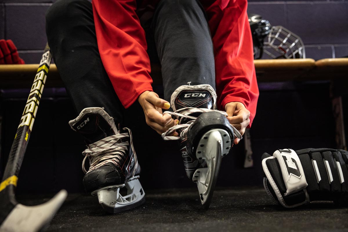 hockey player in a locker room tying his skates with additional hockey gear displayed around him
